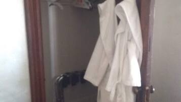 A hotel room with a wooden door, a closet with hanging robes, and a bed with a white bedspread.