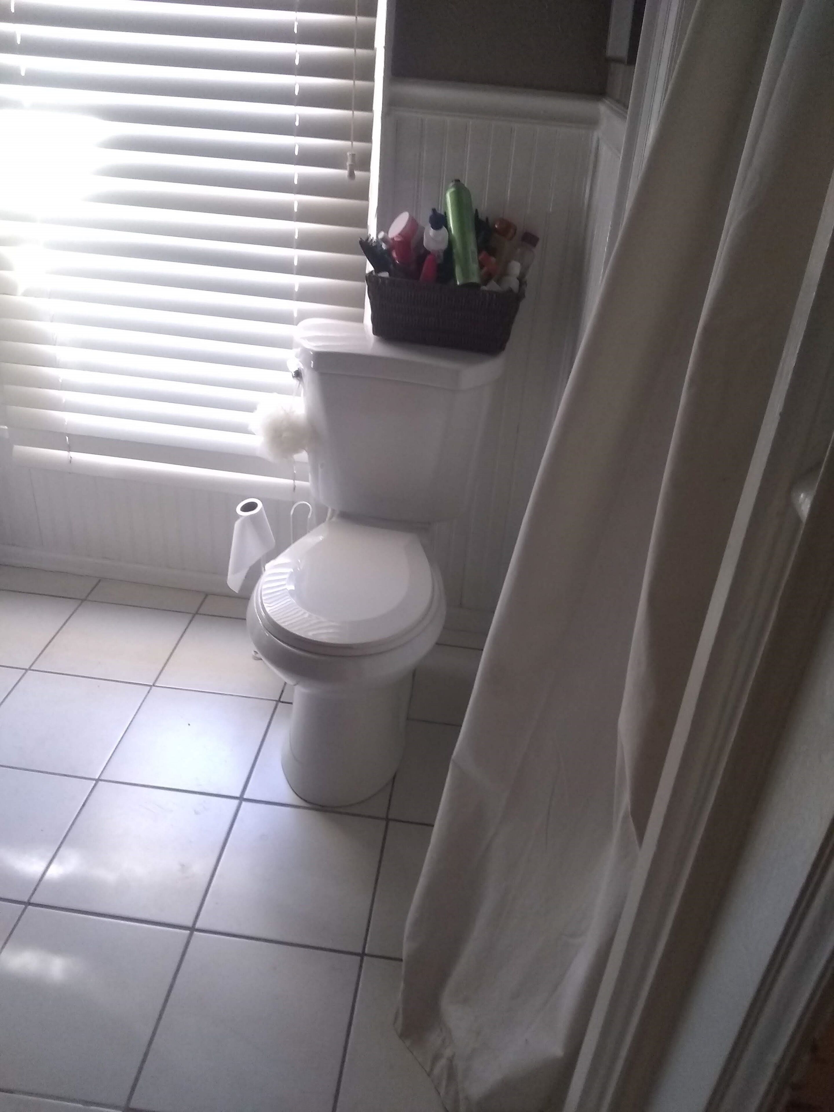 A bathroom with a toilet, a white tiled floor, and a window with blinds.