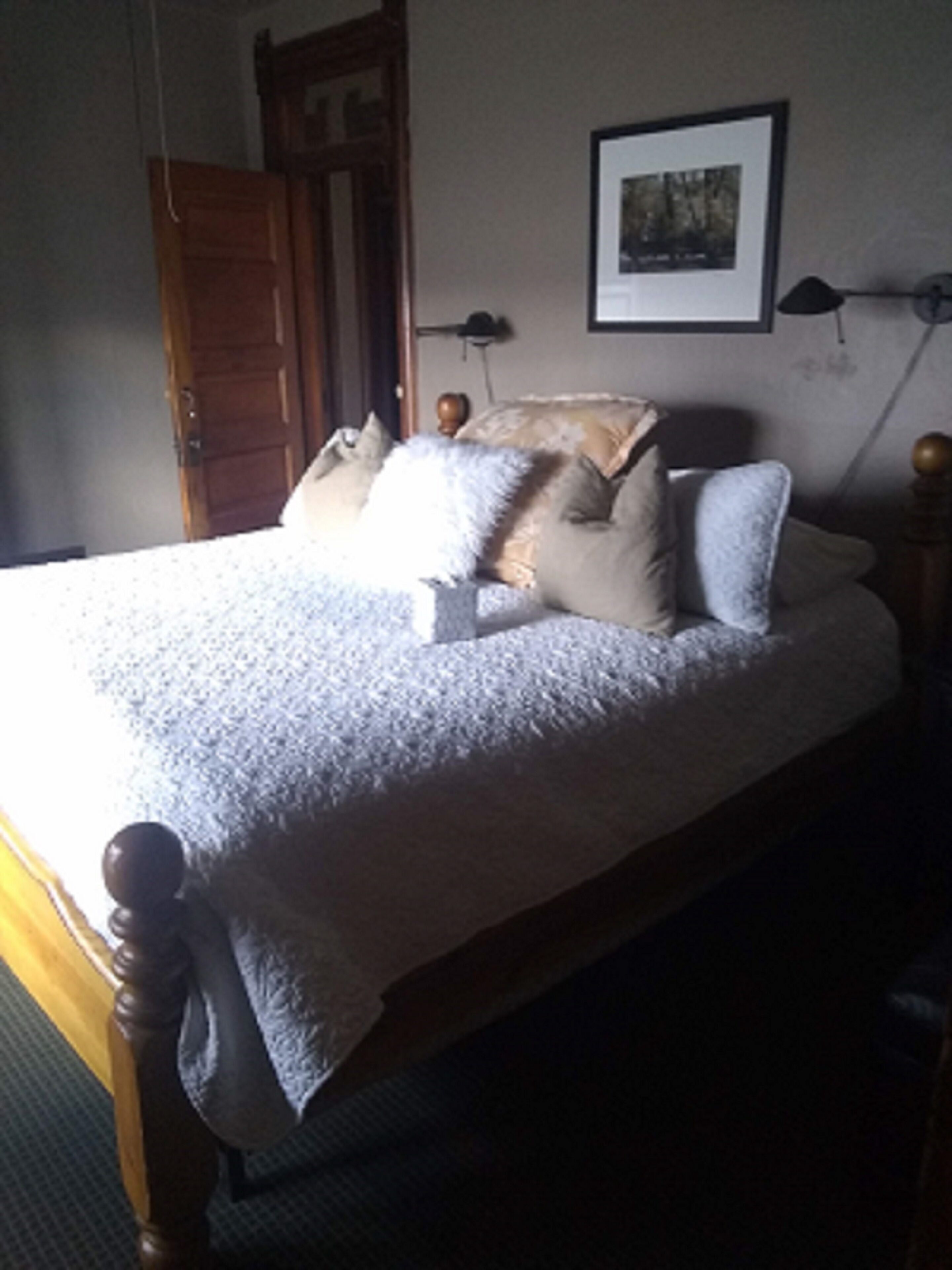 A bedroom with a wooden bed frame, a white bedspread, and several pillows.
