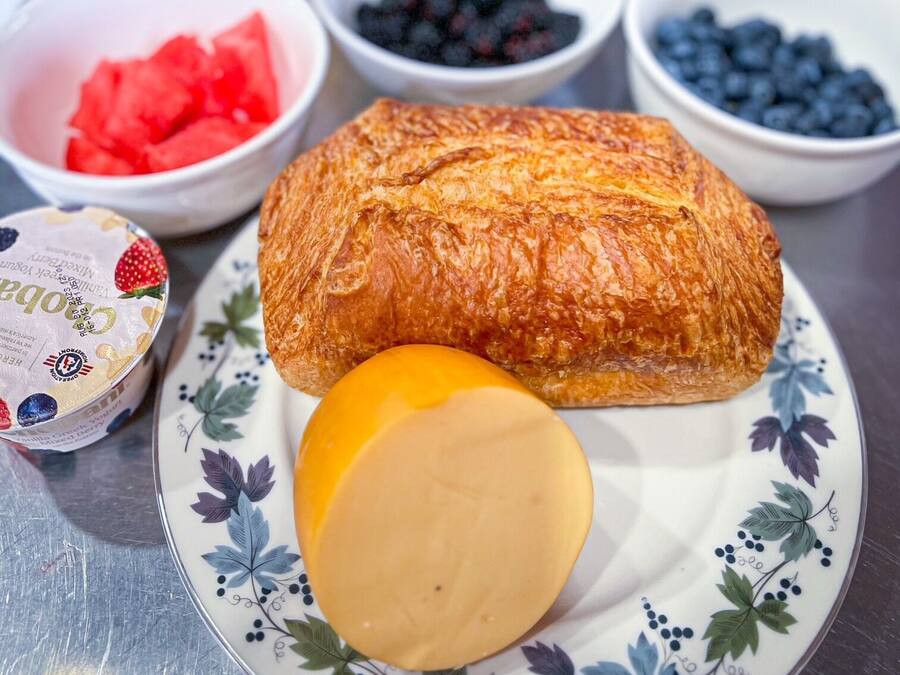 A plate with a croissant, a slice of cheese, and a bowl of blueberries.