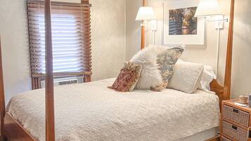 A four-poster bed with a white bedspread, two wall-mounted lamps, and a framed picture on the wall.