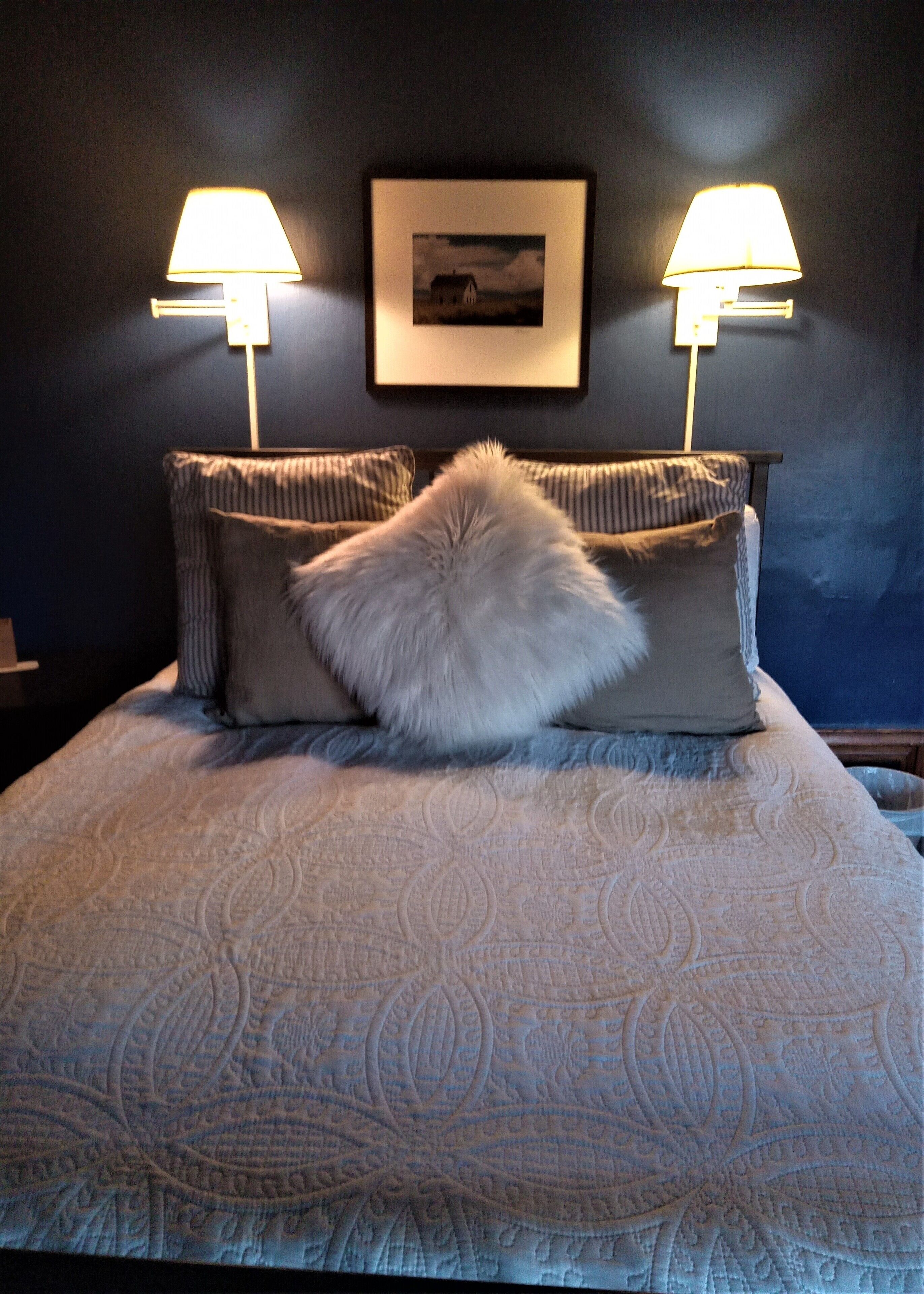 A bed with a patterned bedspread, two pillows, and two wall-mounted lamps.
