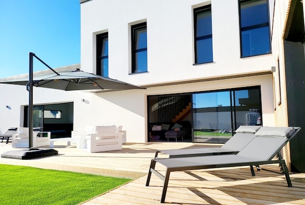 Et moderne hus med en patio med liggestole, et bord og en parasol.
