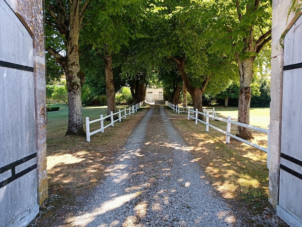 A gravel pathway flanked by white fences and trees, leading to a building with a white facade and black trim. - Beautiful Boathouse by the River (Bourg-Charente)
