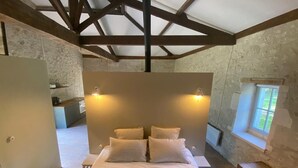 Un dormitorio con una cama grande, vigas de madera, paredes de piedra, una ventana pequeña y un aparador de madera.
