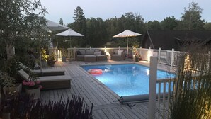 Una terrazza in legno con piscina, circondata da un recinto bianco e mobili da giardino.