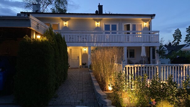Una casa a due piani con un portico anteriore, un ingresso coperto e un piccolo giardino con vasi di piante.