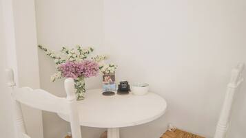 Una mesa blanca con dos sillas de mimbre, un jarrón con flores y un cuadro en la pared.
