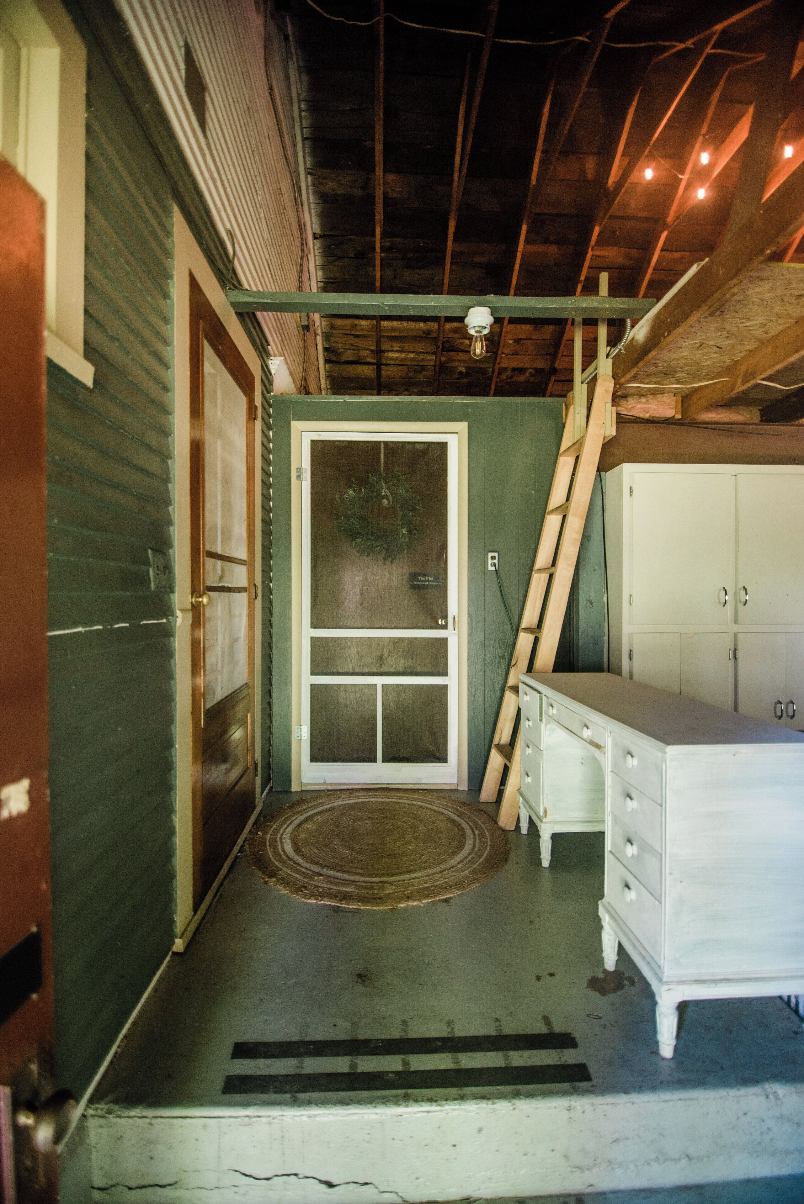 Un petit hall d’entrée avec une porte, une échelle en bois et une commode blanche.