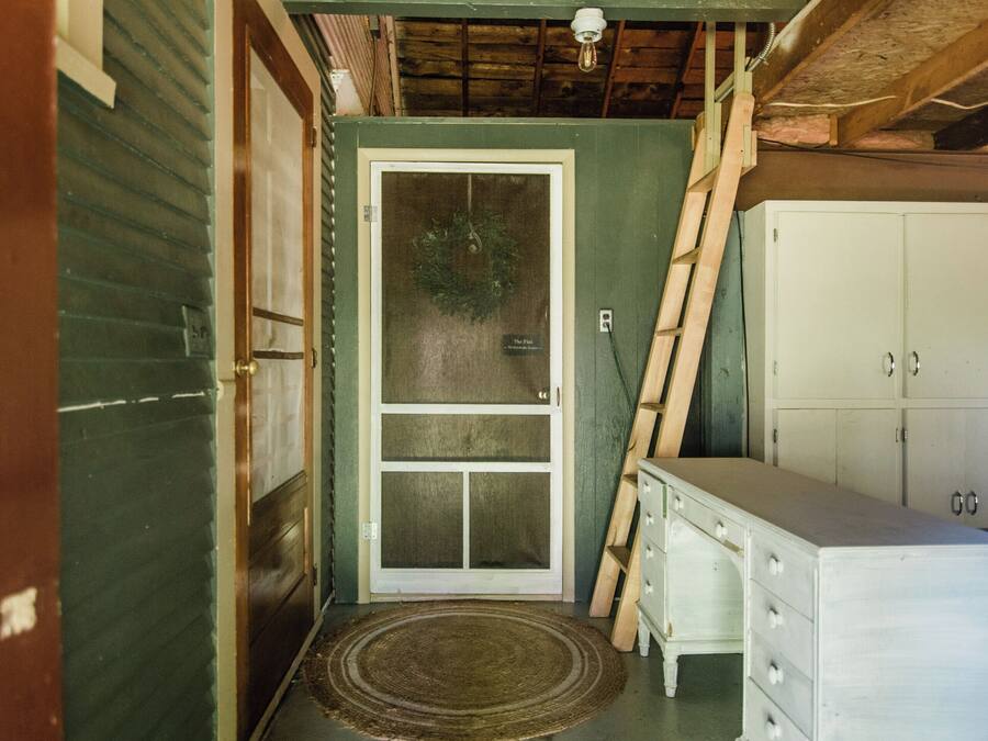 Un petit hall d’entrée avec une porte, une échelle en bois et une commode blanche.