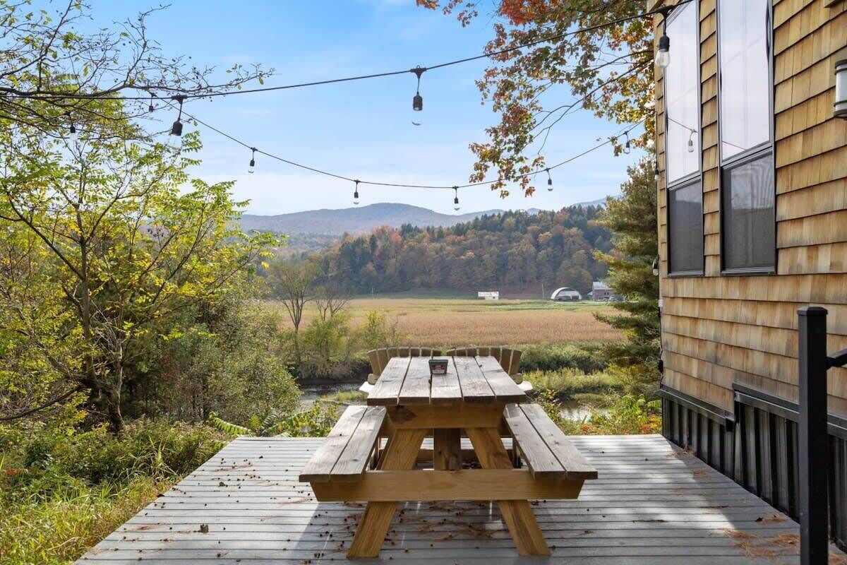Eine Holzterrasse mit Picknicktisch, mit Blick auf eine malerische Landschaft aus Bäumen und Hügeln.