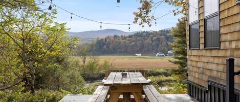 Eine Holzterrasse mit Picknicktisch, mit Blick auf eine malerische Landschaft aus Bäumen und Hügeln.