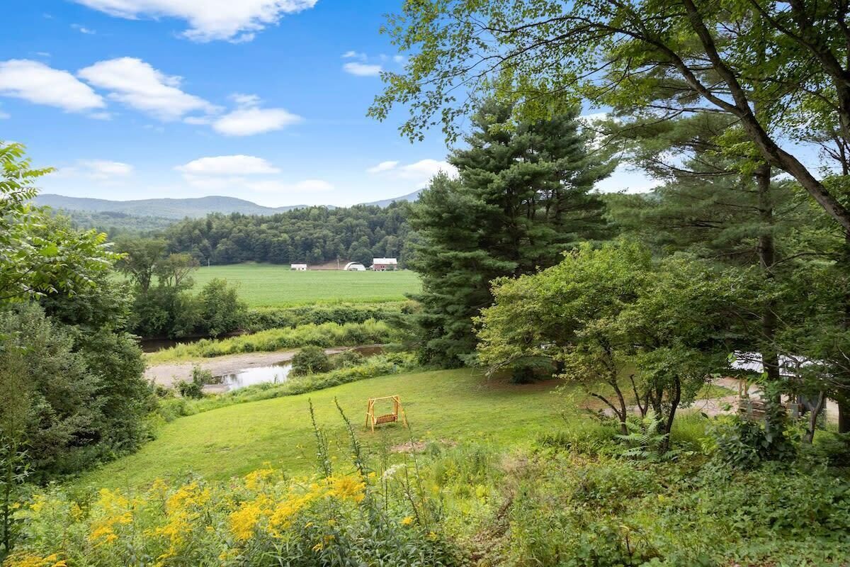 A rural landscape with a grassy field, a swing, and a distant view of a barn and hills.
