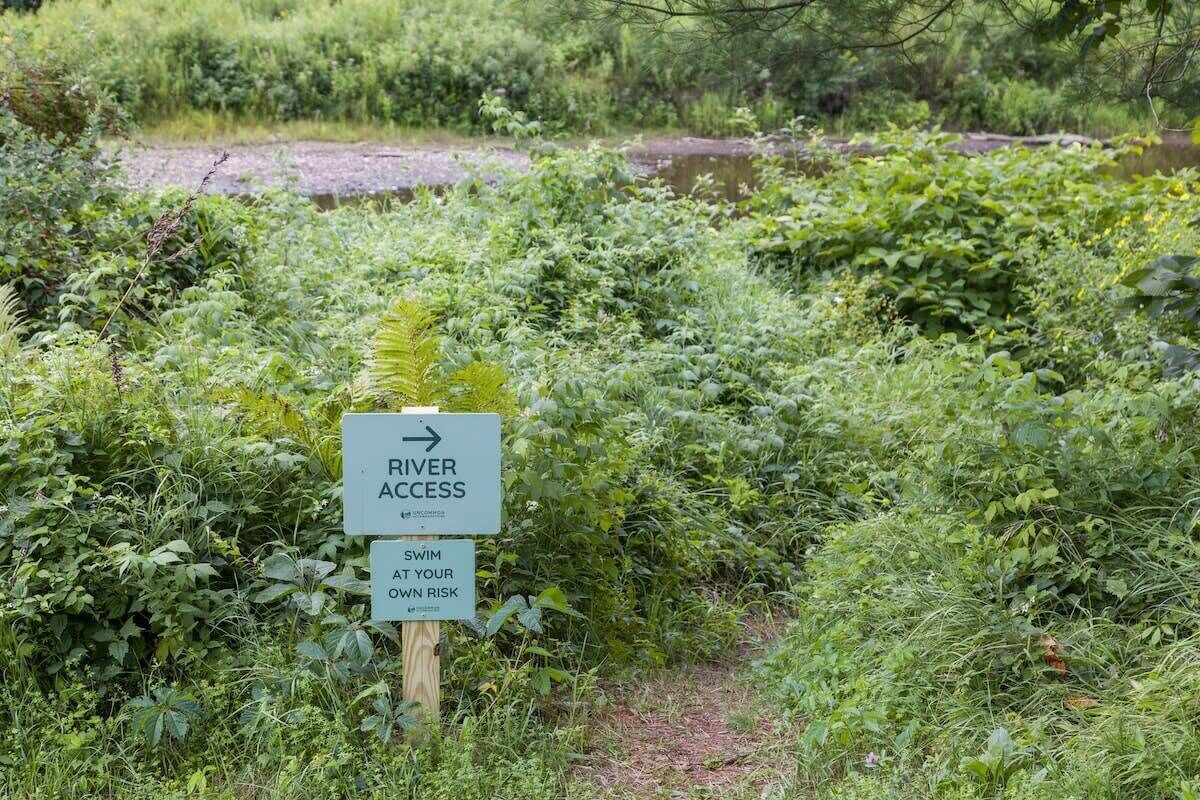 Un panneau indiquant l’accès à la rivière et avertissant que la baignade se fait à vos propres risques.