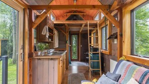 Una cabaña con cocina, comedor y una sala de estar acogedora con sofá y almohadones.