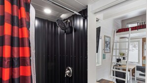 Una habitación con puerta negra, ducha, litera, escritorio y una silla.