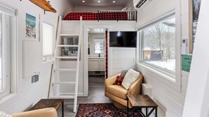 Una habitación compacta con cama alta, sofá, mesita y televisor.