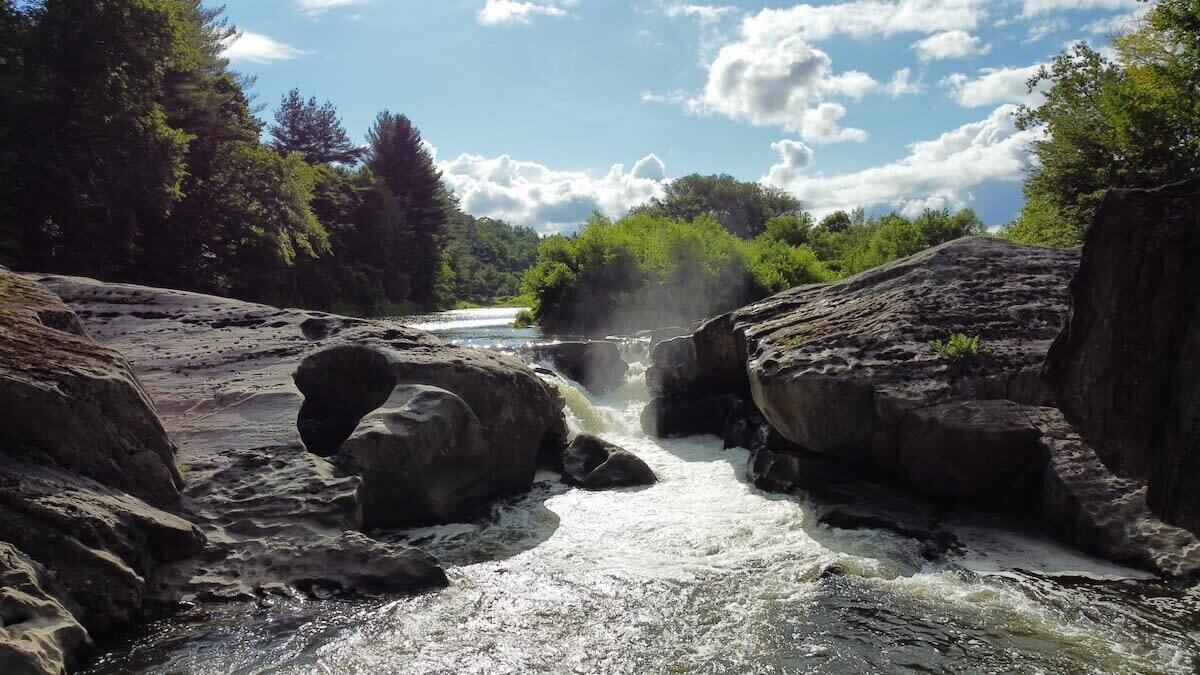 Een natuurlandschap met een rivier die door een rotsachtig terrein kronkelt, omgeven door weelderige begroeiing.