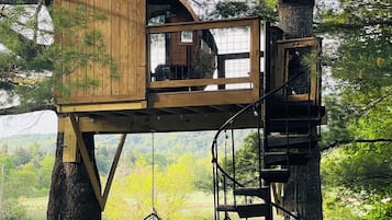 A treehouse with a wooden exterior, a circular viewing window, and a hanging chair.