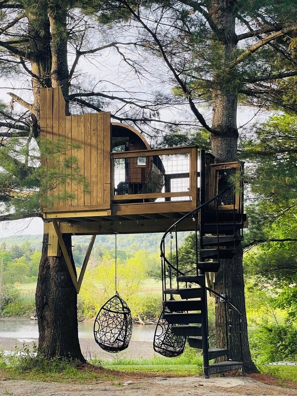 A treehouse with a wooden exterior, a circular viewing window, and a hanging chair.