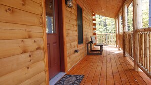A wooden cabin with a porch, a door, and a bench.