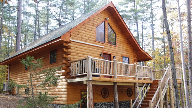 A log cabin with a balcony and a staircase leading to the entrance.
