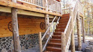 A wooden staircase leading to a balcony with a stone wall and wooden deck.