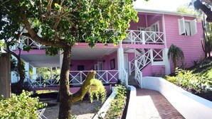 A pink building with a white balcony and a tree in the foreground. - "Beyond" a paradise in Barbados (Cattlewash)