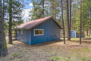 Situated in a forested area, this cabin features a front porch with a bench and a small porch area with a railing.
