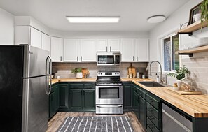 Modern kitchen with stainless steel appliances, wooden countertop, and a window above the sink.