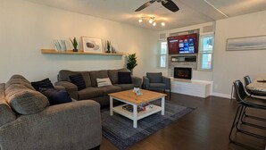 A modern living room with a grey sofa, a wooden coffee table, a fireplace, and a TV mounted on the wall.