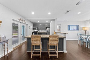 A modern kitchen with a central island, bar stools, and a dining area with a table and chairs.