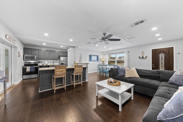 A modern kitchen with dark cabinets, a central island, and a dining area with blue chairs.