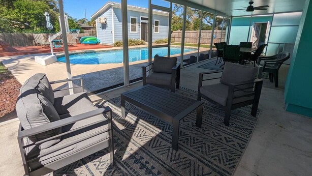 A covered patio with outdoor furniture, a pool, and a view of a house.