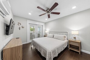A bedroom with a bed, nightstands, a ceiling fan, and a TV mounted on the wall.