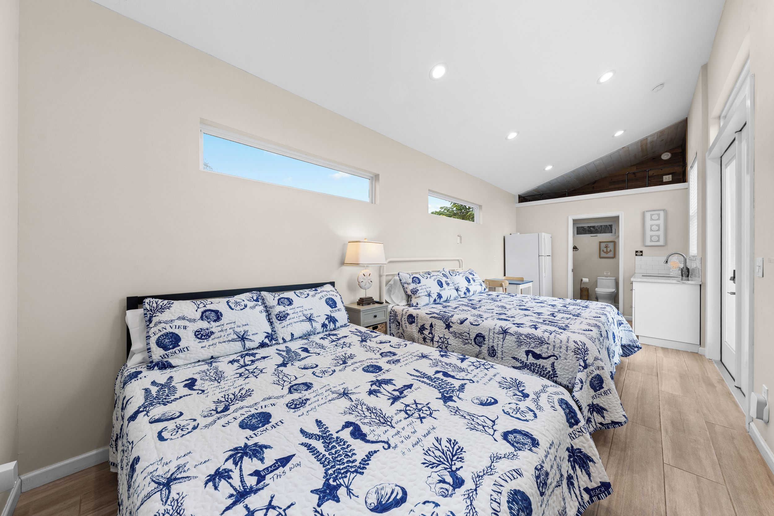 A bedroom with two beds, a nightstand, a lamp, and a window.