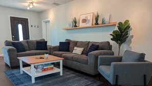 A living room with a grey sofa set, a wooden coffee table, a blue rug, and a potted plant.