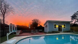 A backyard with a swimming pool, a basketball hoop, and a small house.
