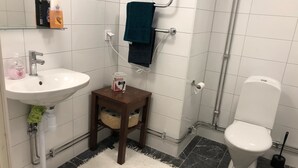 Ein Badezimmer mit einem weißen Waschbecken, einem kleinen hölzernen Hocker mit Toilettenpapier, einem Handtuchhalter und einer Toilette.