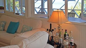 Ein weißes Sofa mit türkisfarbenen Kissen, ein Holztisch mit einer Lampe und Alkoholflaschen.