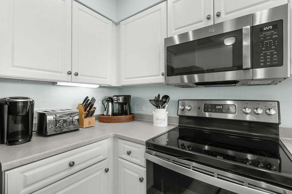 A kitchen with white cabinets, a stainless steel microwave, a toaster, and a coffee maker.