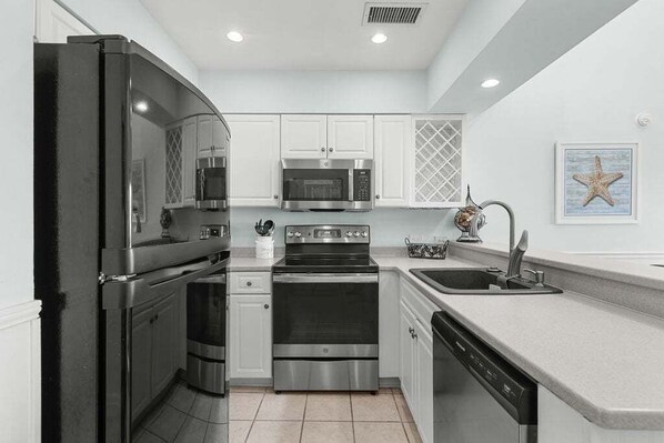 A modern kitchen with stainless steel appliances, white cabinetry, and a built-in dishwasher.