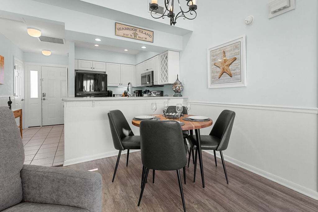 A modern kitchen with white cabinets, a microwave, and a dining area with a wooden table and four chairs.