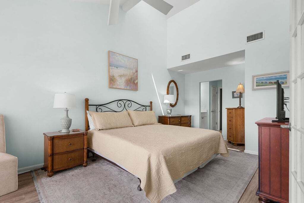 Un dormitorio con cama, mesitas de noche, cómoda, espejo y un cuadro en la pared.