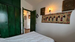 Ein Schlafzimmer mit Bett, grünem Wandschrank, Wandleuchte und Wandteppich.