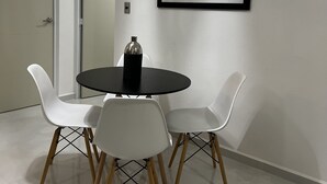 A dining area with a round table, four white chairs, a black tablecloth, a bottle, and a framed picture on the wall. - 5 minutes from the beach and pool (manzanillo)