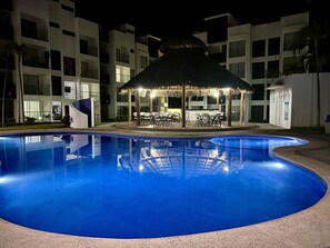 Una piscina con un quiosco de techo de paja y sillones de descanso.