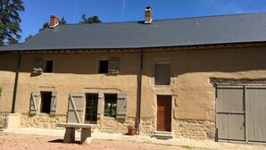 A two-story building with a stone facade, multiple windows with shutters, and a grey door. - Le Potager - Martigny-le-comte (MARTIGNY-LE-COMTE)