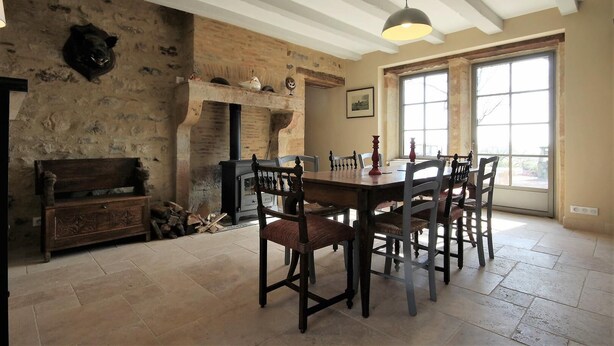 A dining area with a large wooden table, several chairs, a fireplace, and a stone wall. - Le Potager - Martigny-le-comte (MARTIGNY-LE-COMTE)