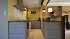 A modern kitchen with a central island, wooden cabinetry, and a stone accent wall. - Le Potager - Martigny-le-comte (MARTIGNY-LE-COMTE)